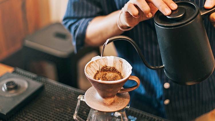 Wasser wird aus einer schwarzen Kanne in einen Kaffeefilter auf einer Keramikkanne gegossen.