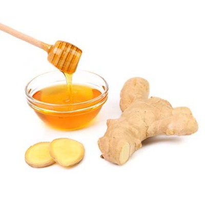 Eine Glas-Schale mit Honig, darin ein Honiglöffel, daneben frischer Ingwer und zwei Ingwerscheiben auf weißem Untergrund.