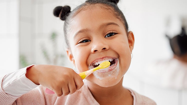 Eine Person in rosa Kleidung hält eine Zahnbürste vor einem unscharfen Badezimmerhintergrund in der Hand.